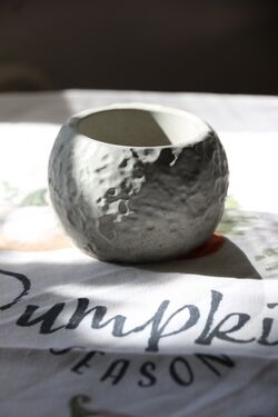 Gömbölyded, kráteres felületű beton tál napfényben, textil terítőn.