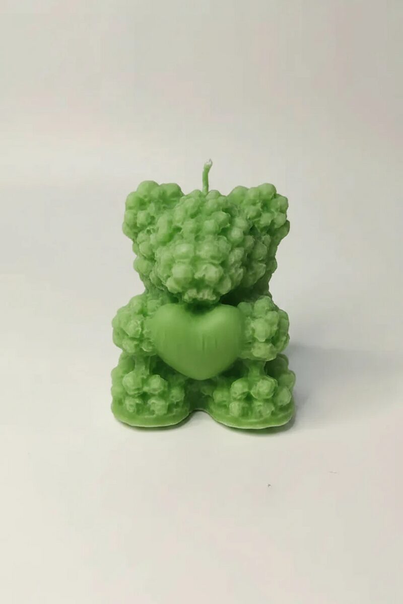 Zöld színű, virágos textúrájú medve alakú szójaviasz gyertya, mely a mancsában egy szív alakot tart.