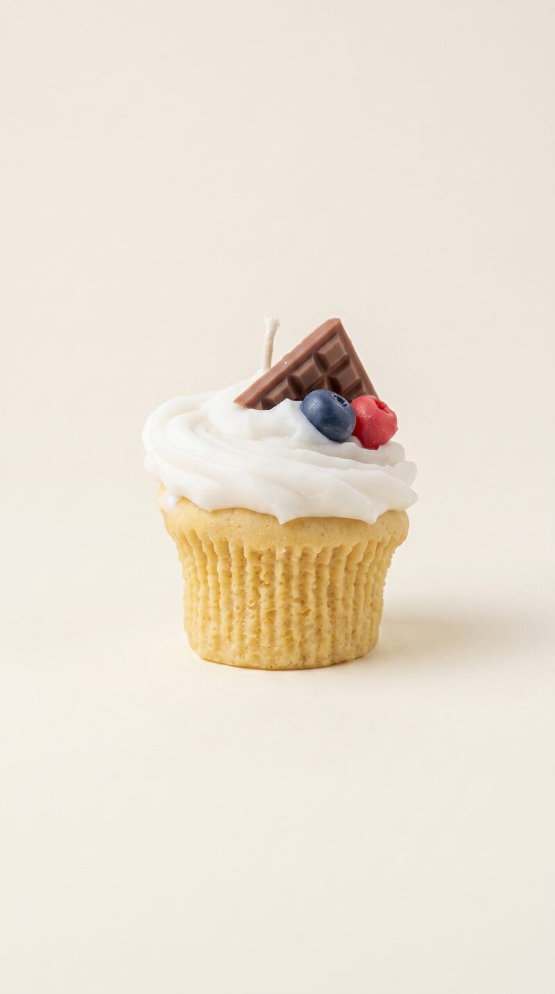 Krémes áfonyás muffin formájú szójaviasz gyertya, fehér krémmel, csokoládéval, áfonyával és málnával díszítve.