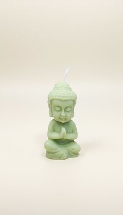 Zöld színű, ülő Buddha alakú szójaviasz gyertya, összetett tenyerekkel, fehér színű mécsessel.