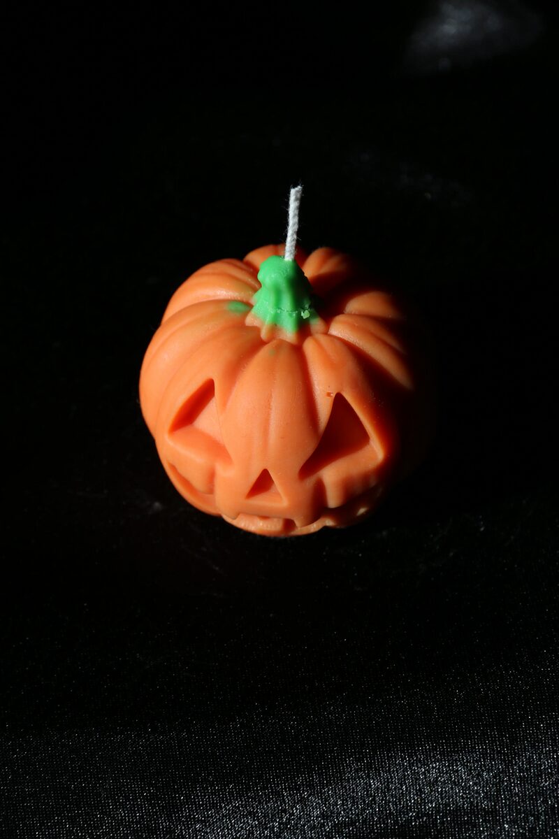 Kis Halloween tök gyertya enyhén oldalról, háromszög szemekkel és fogas mosollyal.