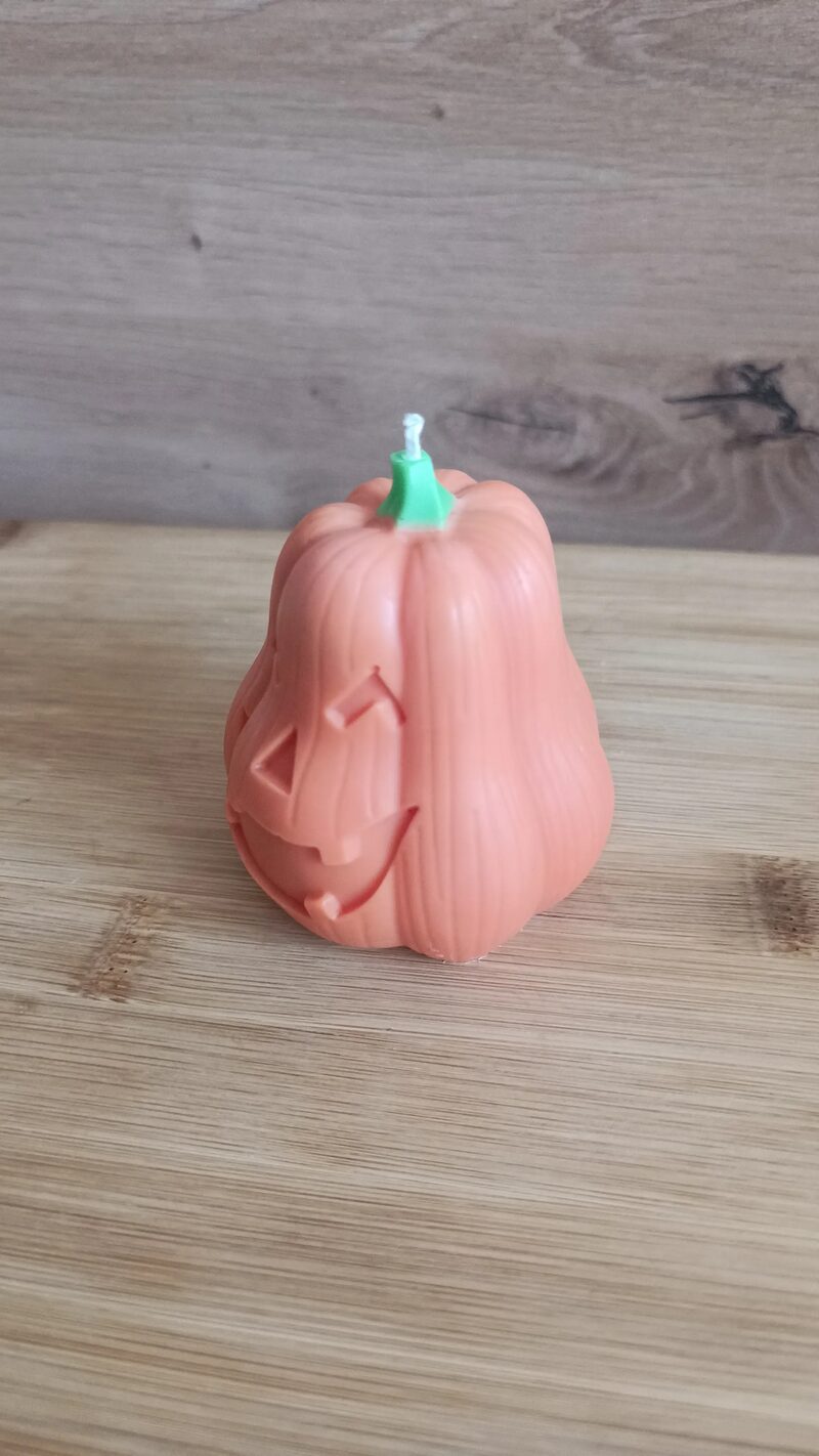 Nagy Halloween tök gyertya oldalnézetből, bordázott tökformával és zöld kanócszárral.