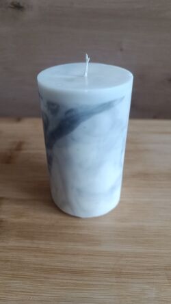 Fehér márványmintás henger alakú szójaviasz gyertya pamut kanóccal, fa asztalon.