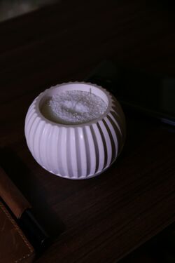 Zen gömb kerámia tál hófehér homokviasszal és pamut kanóccal, sötét fa asztalon.