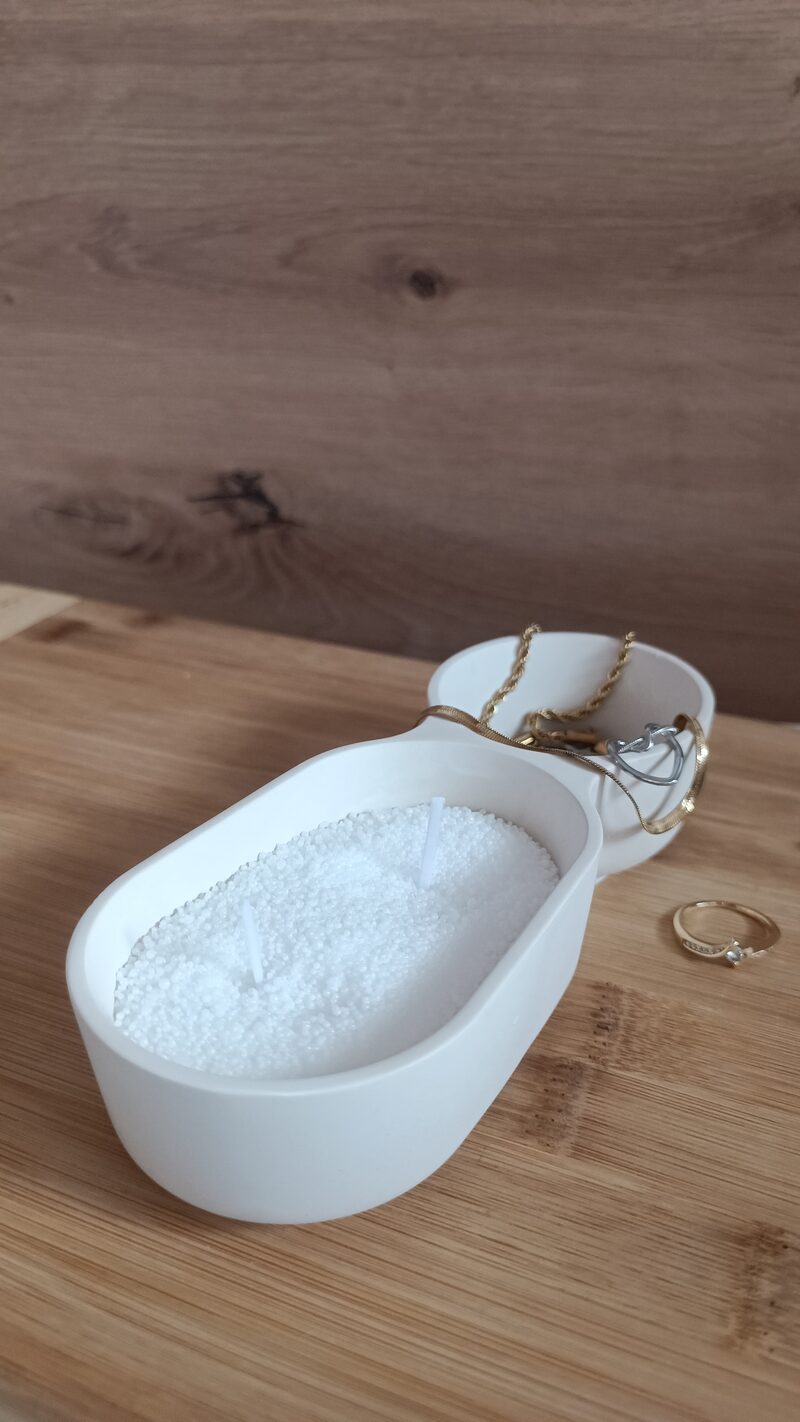 Homokviasszal töltött dupla öböl kerámia tálca két pamut kanóccal, mellette gyűrű és aranyszínű láncok.